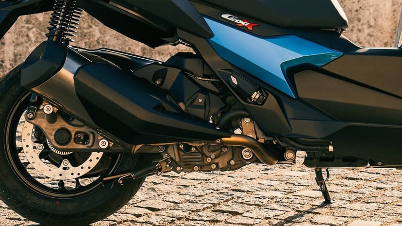 Rear mechanical details of a BMW C400X scooter showing exhaust, engine, and wheel on a sunlit cobblestone path.