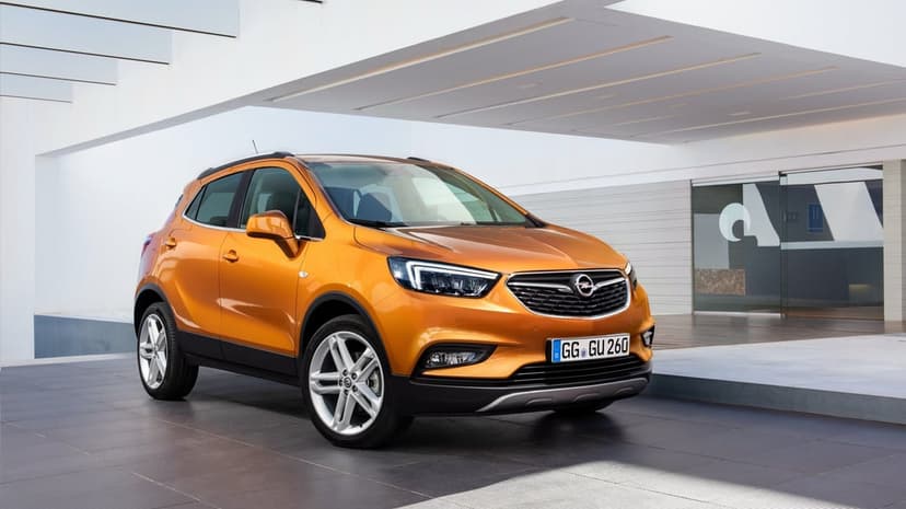 Metallic orange Opel Mokka X SUV parked in front of a minimalist white building with sharp geometric shadows.