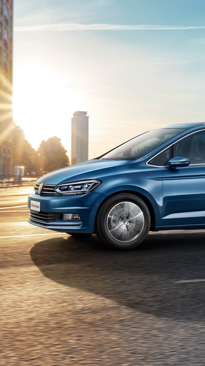 Blue Volkswagen driving on urban road during sunrise with golden sunlight flare and motion blurred wheels.