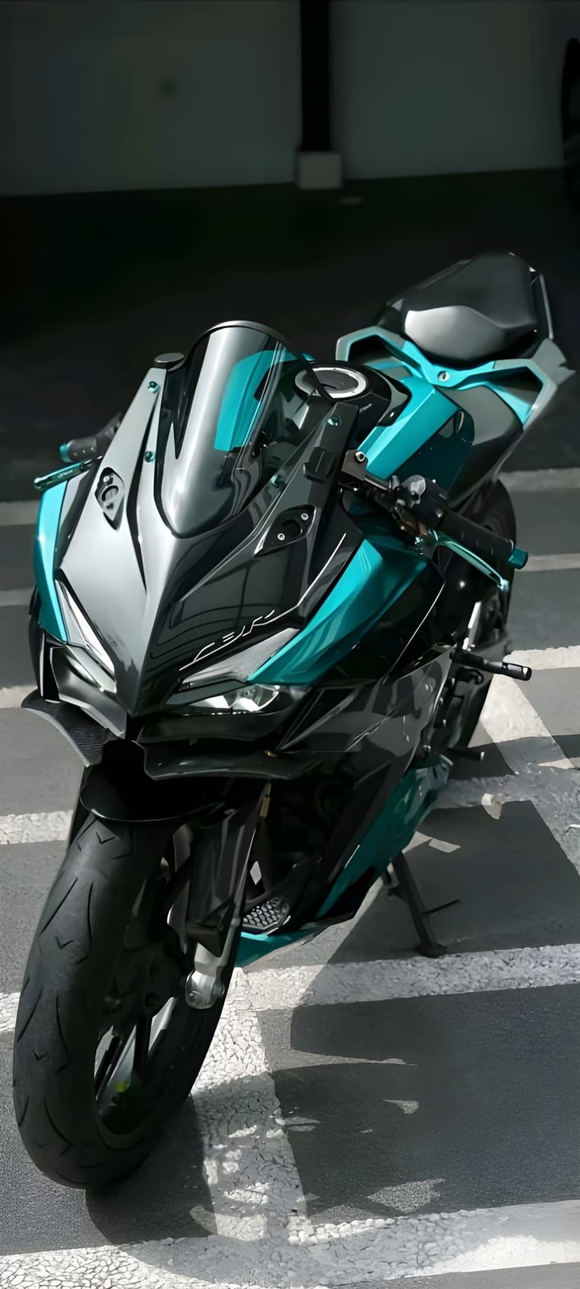 Teal and silver sportbike motorcycle with aggressive headlights and a tinted windscreen parked on a grey road.