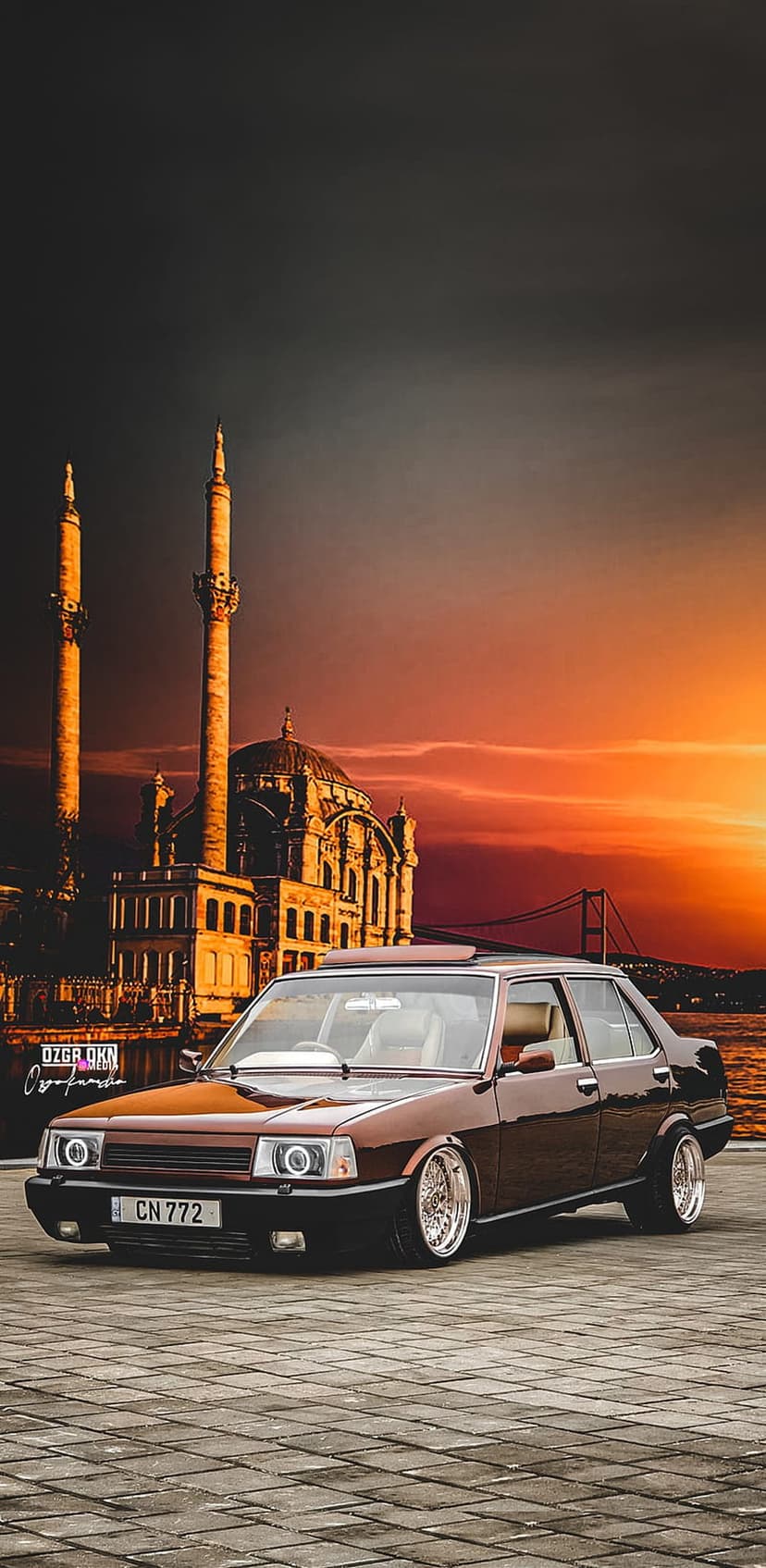 Brown modified Tofaş Şahin car parked near a Turkish mosque and bridge under a vibrant orange sunset sky.