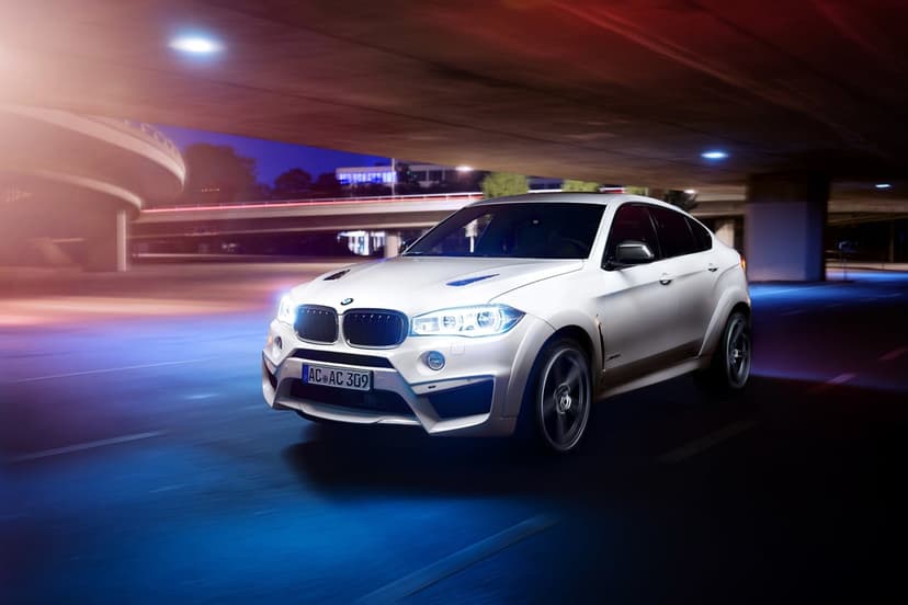 White BMW X6 M SUV driving through a neon-lit urban tunnel at night with visible motion blur on the wheels.