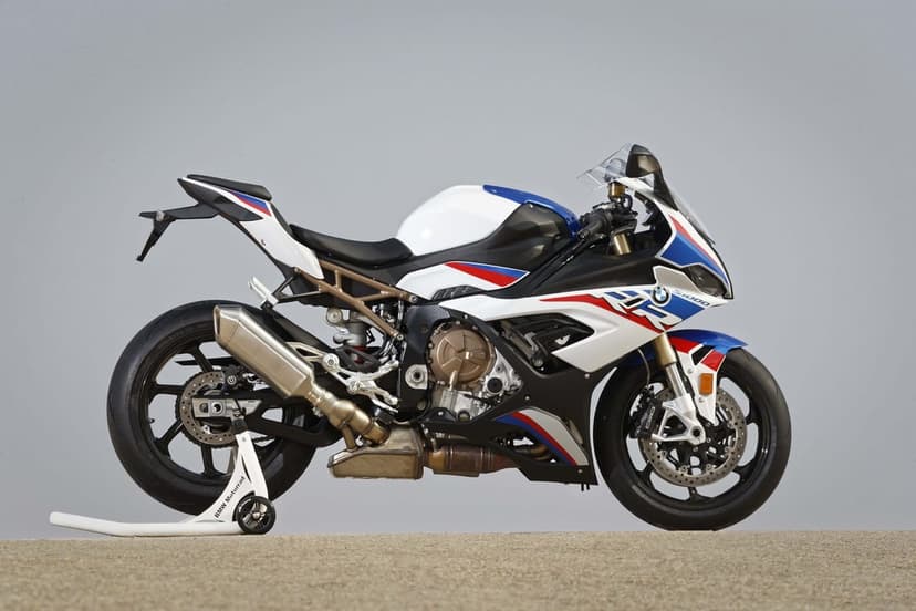 BMW S1000RR sportbike in M Sport colors on a rear stand against a grey background and sandy ground.