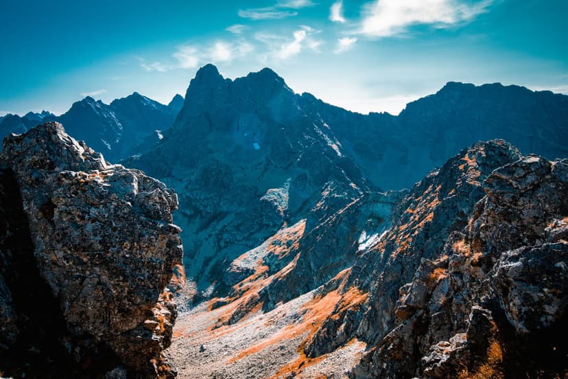 Snow-capped mountain peaks catch golden sunset light beneath a deep blue sky with faint wispy clouds.