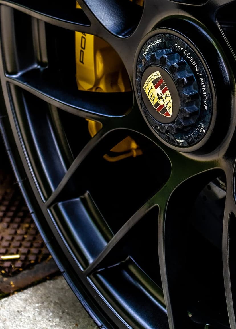 Porsche wheel with a yellow brake caliper and centerlock nut featuring the iconic crest on a black alloy rim.