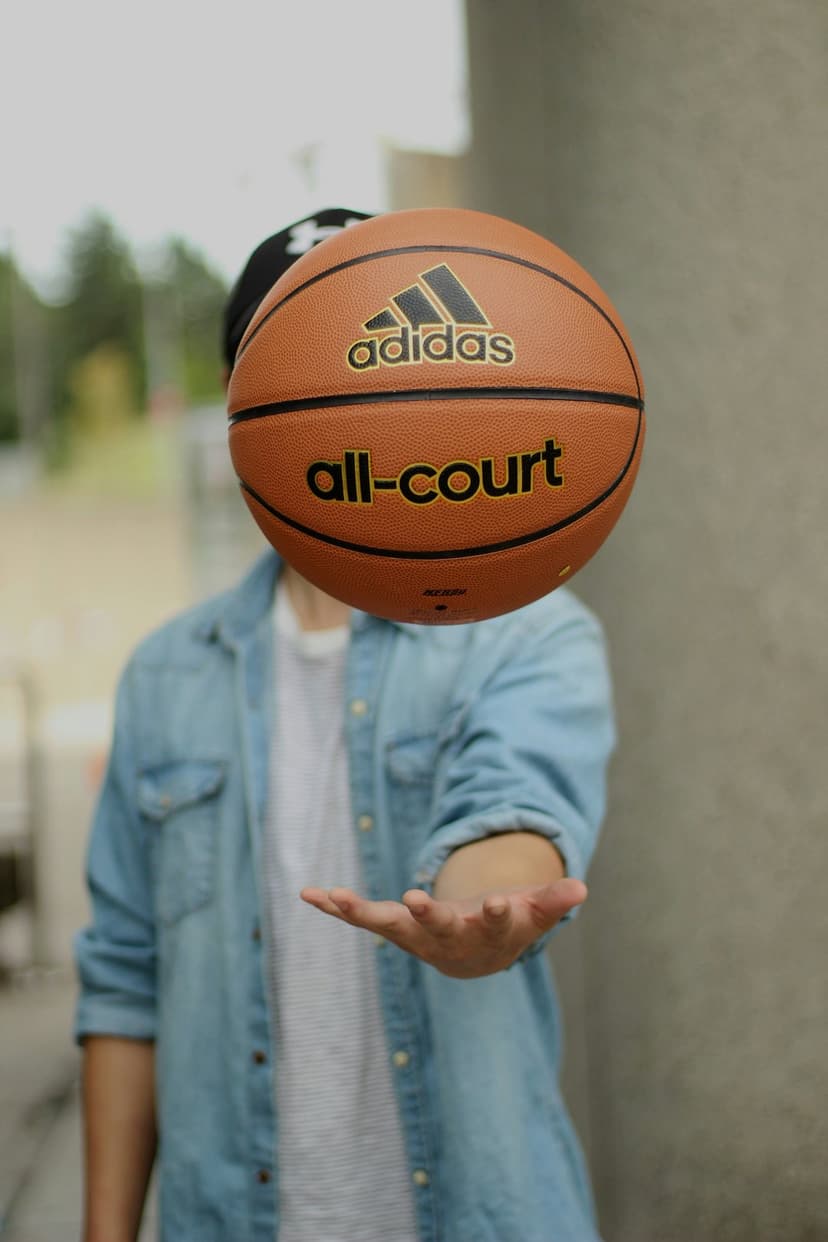 Basketball suspended in the air near a person's hand with a blurred urban wall and denim shirt in background.