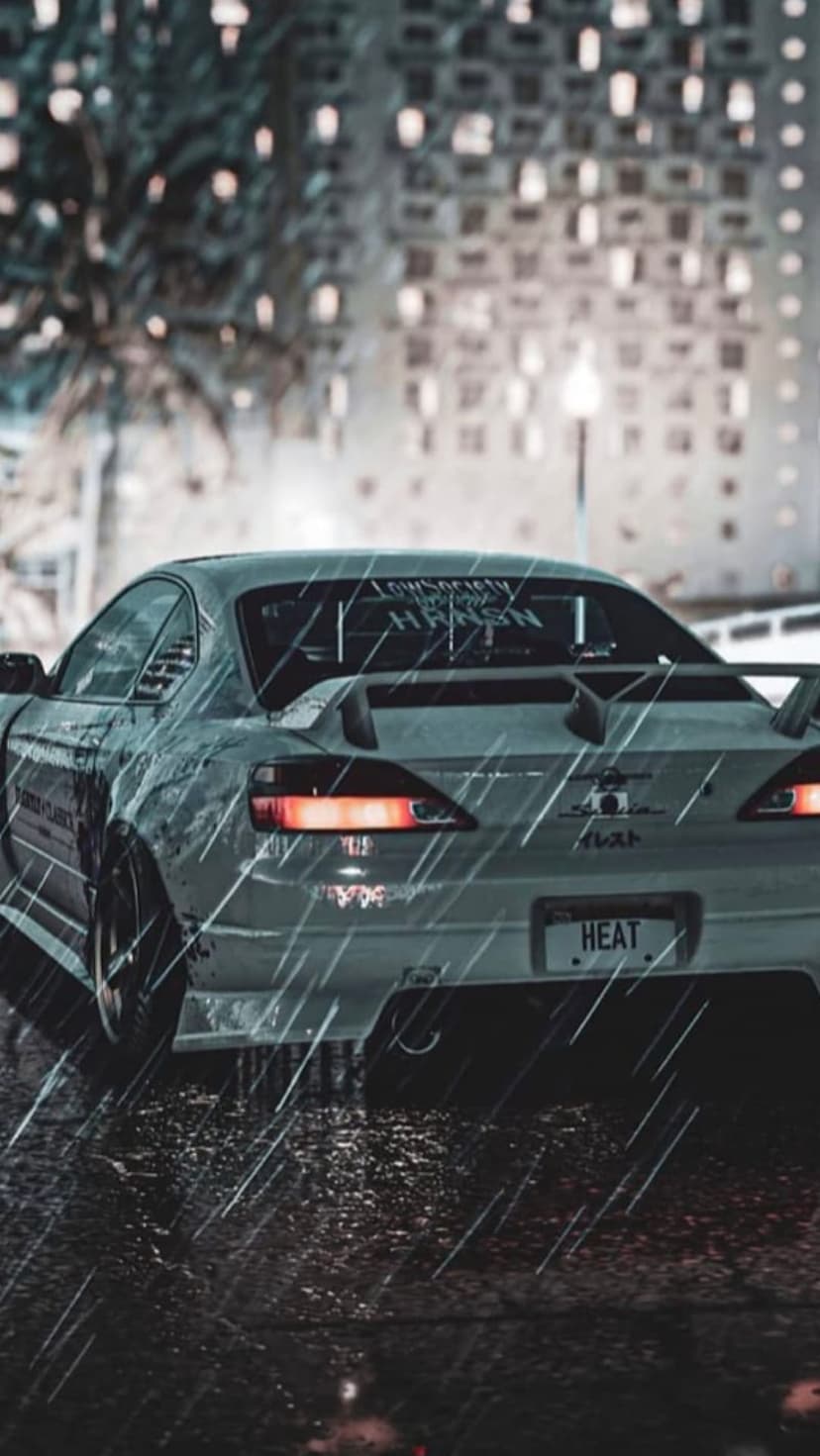 Modified JDM car with a large rear spoiler parked on a wet city street at night under neon reflections.