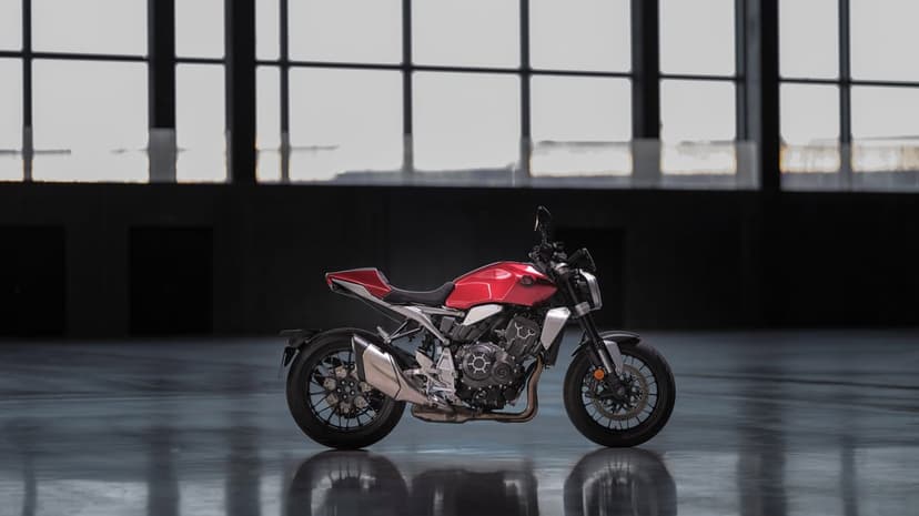 Red modern naked motorcycle parked in a dark industrial hangar with large windows and floor reflections.