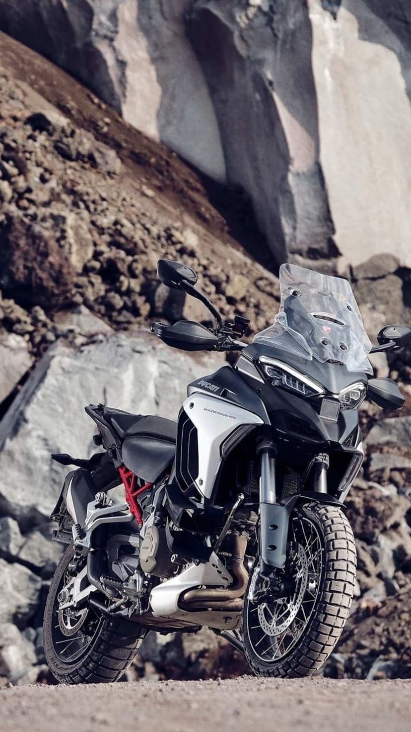 Ducati Multistrada V4 motorcycle parked on a gravel path surrounded by tall orange rock cliffs and dry terrain.