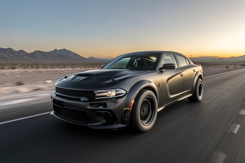 Matte black Dodge Charger widebody speeding on a desert road against a glowing golden hour sunset horizon.