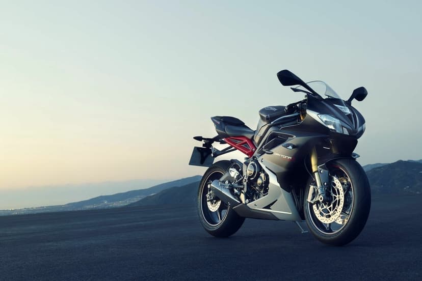 Matte black Triumph Daytona 675R motorcycle parked on asphalt with mountains and twilight sky background.