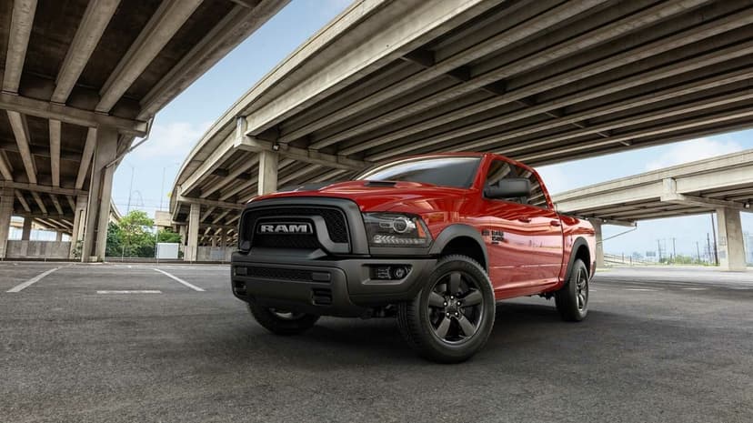 Red RAM 1500 pickup truck parked under concrete highway overpasses on an asphalt lot in bright daylight.