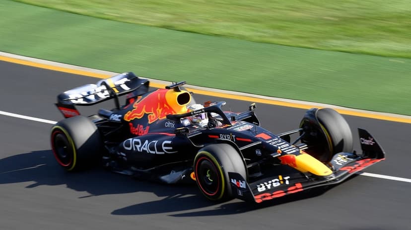 Red Bull RB18 F1 car racing on dark asphalt with motion-blurred green grass and sharp daylight shadows.