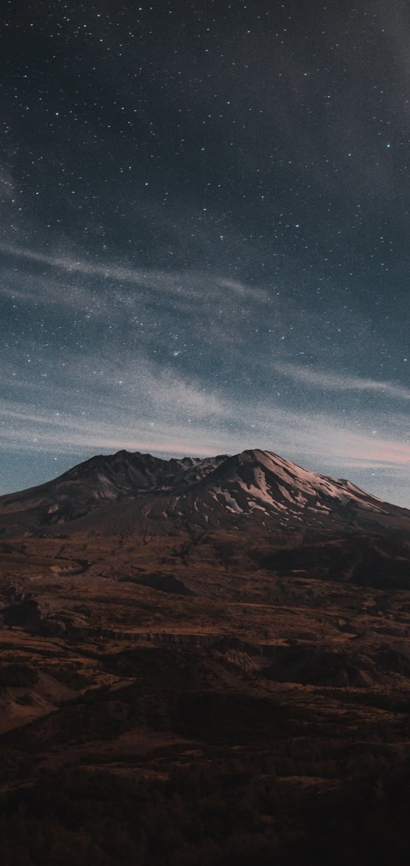 Jagged mountain peak silhouetted against a dense field of glowing stars and wispy cosmic stardust in a dark sky.