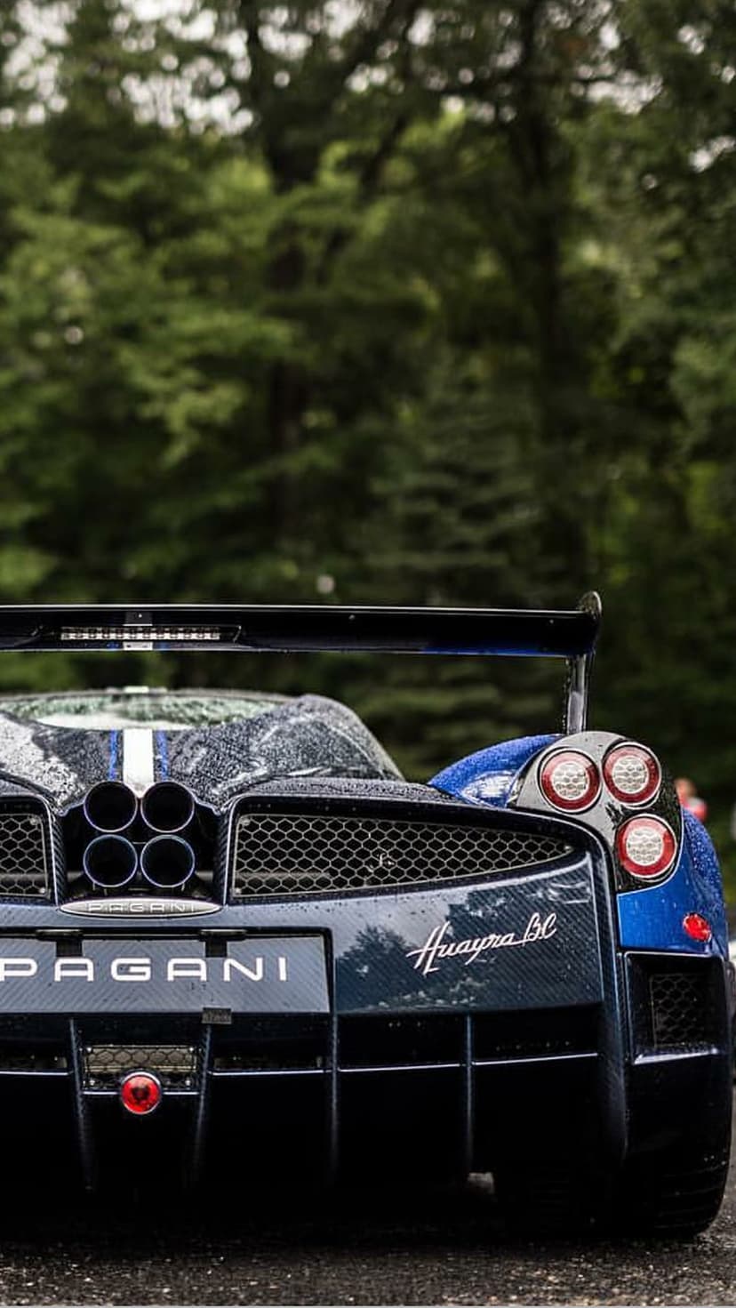 Pagani Huayra BC rear view with raindrops, quad exhaust pipes, and carbon fiber details against green trees.
