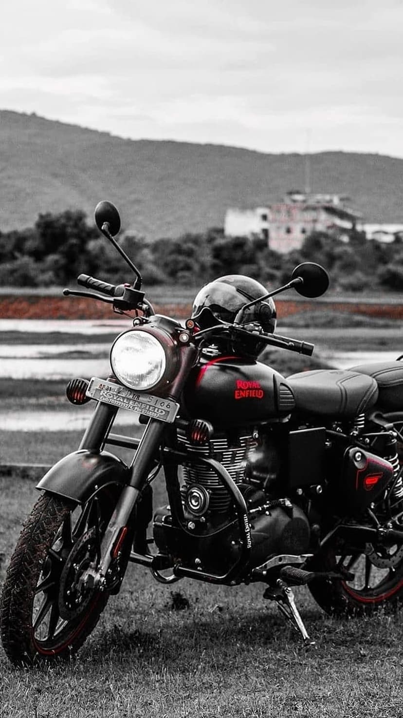 Royal Enfield motorcycle with a black helmet on the handlebars parked in a vast green field under a cloudy sky.