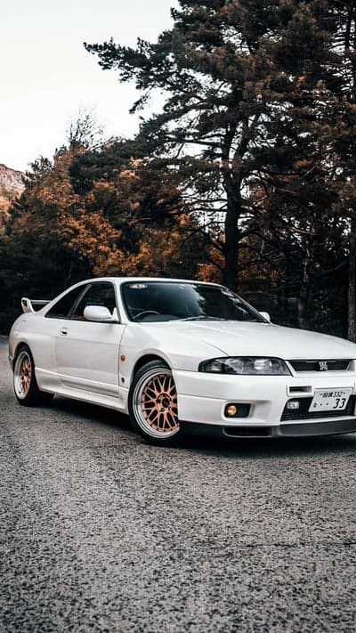 White Nissan Skyline R33 GT-R on a tree-lined road
