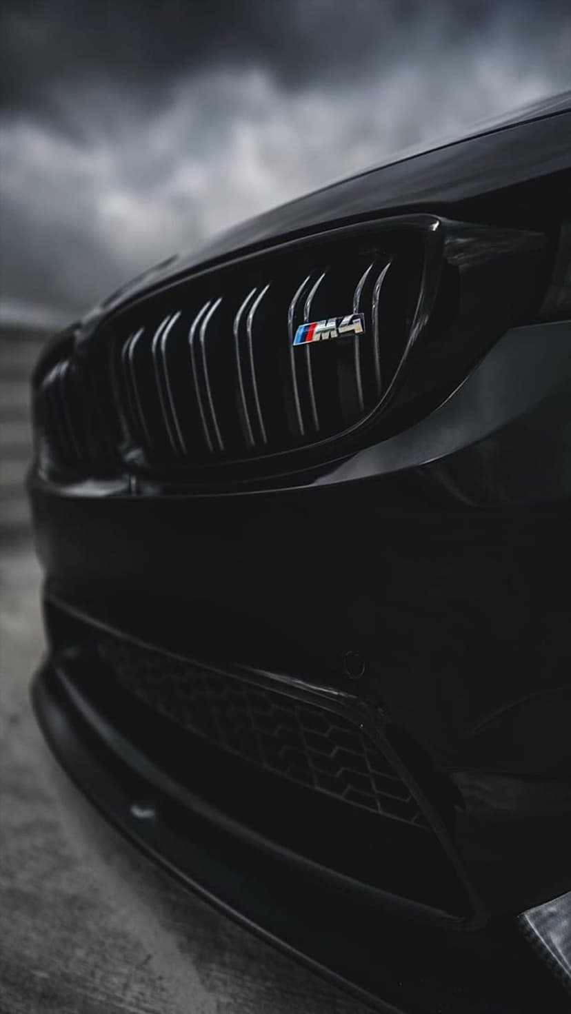 BMW M4 front grille and tricolor M badge under a dark cloudy sky in a low-angle vertical automotive photograph.