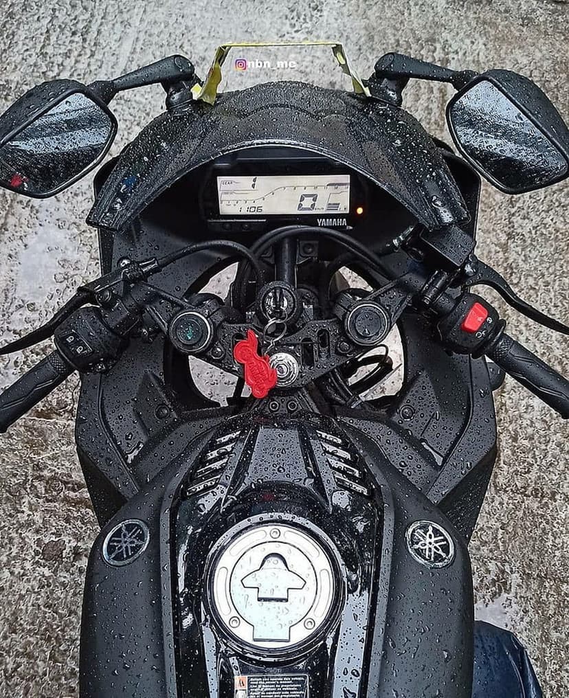 Black Yamaha R15 motorcycle with water droplets on the fairing and digital dashboard during a rainy day.