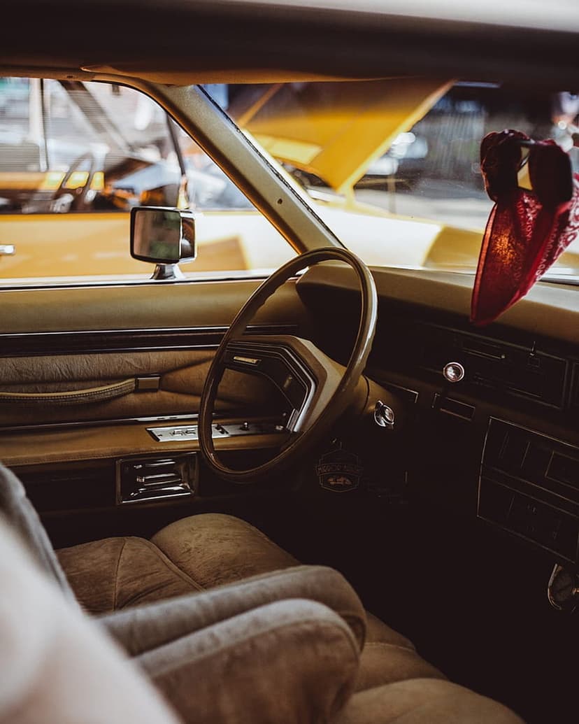 Brown leather car seats and a classic steering wheel are illuminated by sunlight inside a vintage vehicle cabin.
