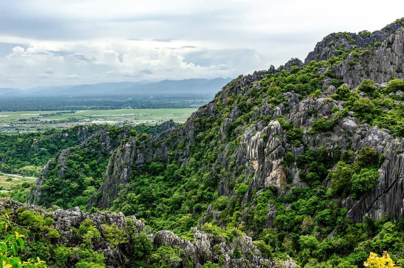 Sharp green mountain ridges overlook a wide flat valley under a grey cloudy sky in a vertical nature vista.