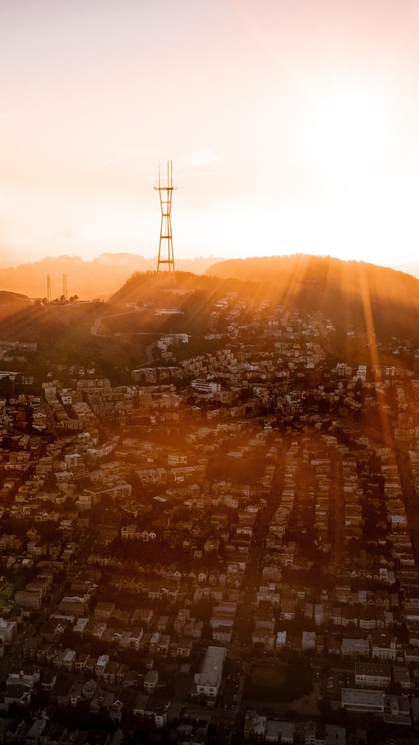 Sutro Tower rises above the San Francisco urban sprawl as golden sunset rays illuminate the hazy city skyline.