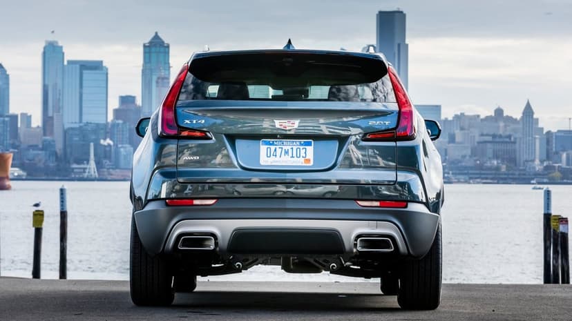 Rear view of a dark blue Cadillac XT4 parked on a pier with a city skyline and water in the background.