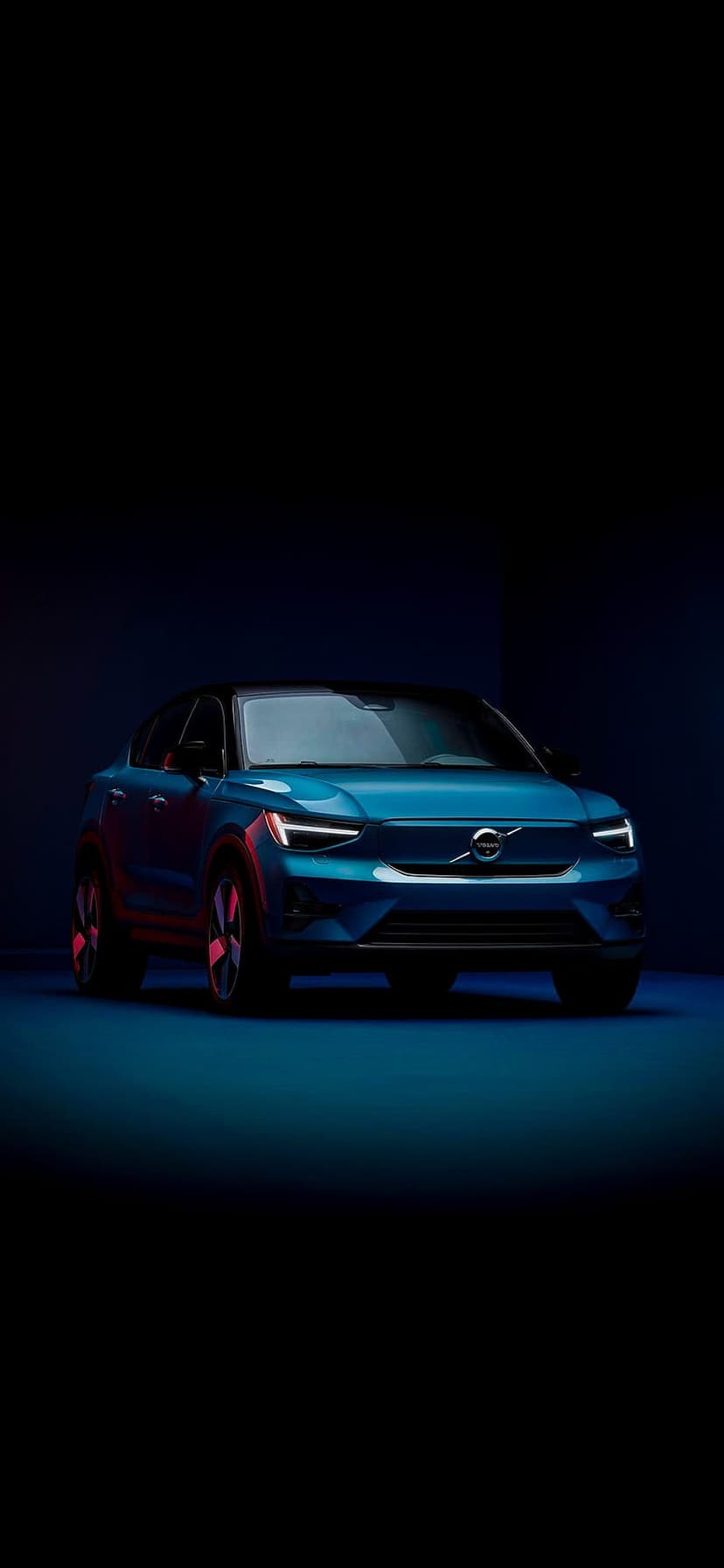 Blue Volvo XC40 Recharge SUV parked in a dark studio with dramatic lighting highlighting its front and side profile.