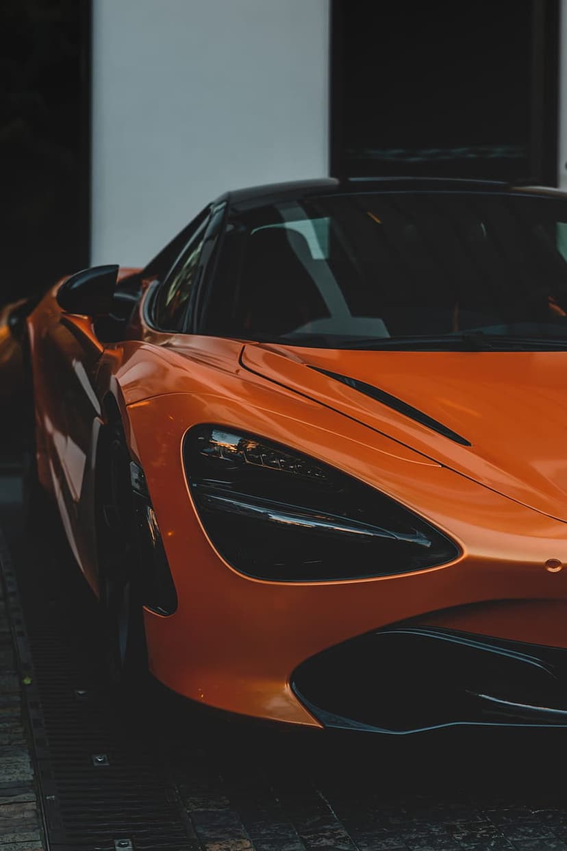 Orange McLaren supercar front view with glowing LED headlights and a low-profile aerodynamic carbon fiber body.