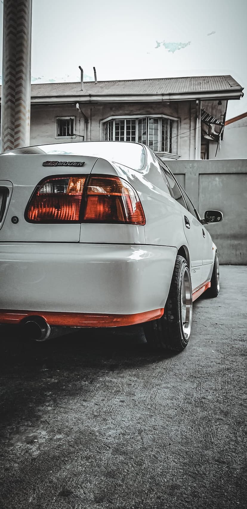 White Honda Civic EG with a Mugen body kit parked on concrete with an orange front lip and exhaust visible.