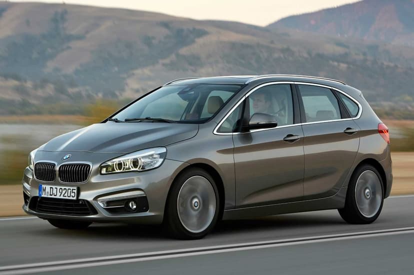 Silver BMW 2 Series Active Tourer driving on a highway with rolling hills in the background at dusk.