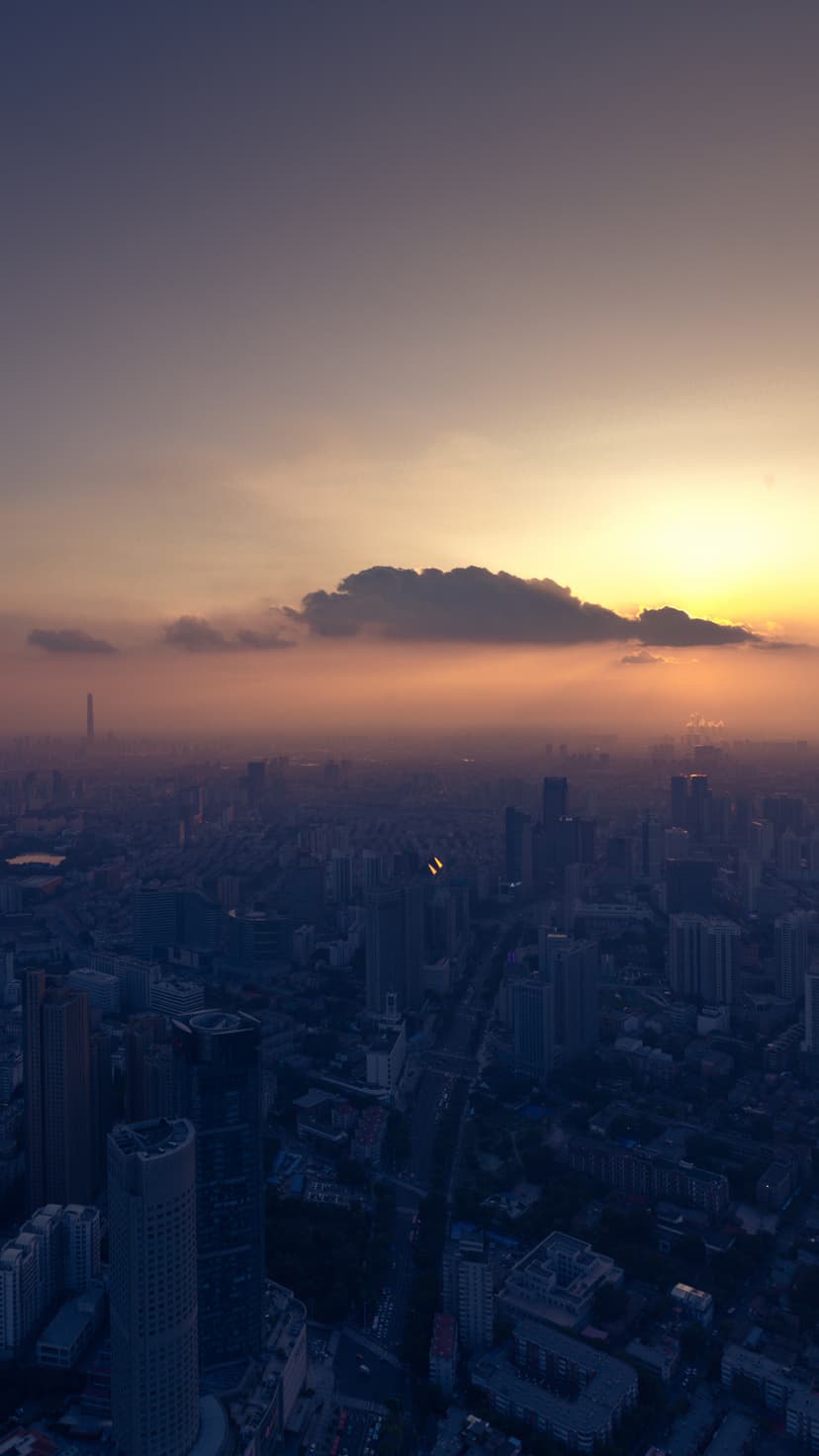 City skyscrapers emerge through a thick golden haze during sunrise, seen from an elevated aerial perspective.