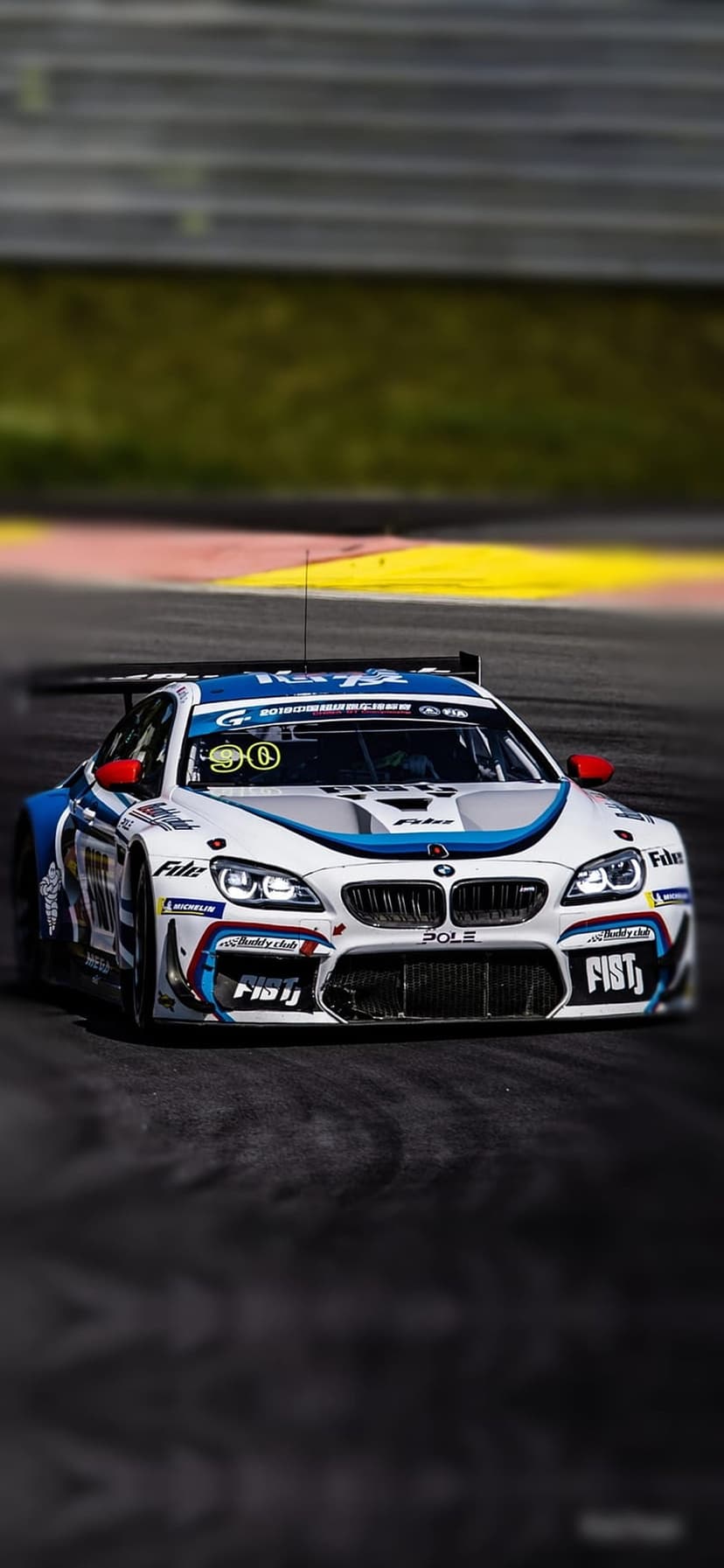 BMW M6 GT3 race car with blue and white decals speeds on a gray track with its large rear wing in focus.