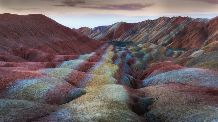 Zhangye Danxia sandstone mountains display vibrant layered mineral colors across a vast panoramic landscape.