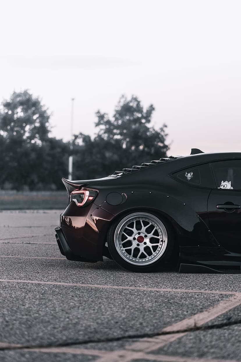 Modified black sports car featuring silver multi-spoke wheels and widebody flares from a low rear perspective.