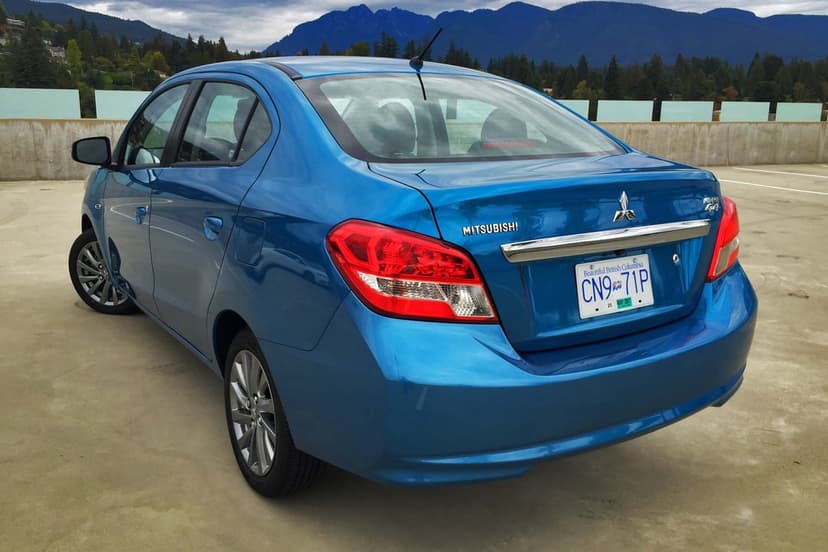 Rear view of a blue Mitsubishi Mirage G4 sedan parked on a concrete lot with green mountains in the background.