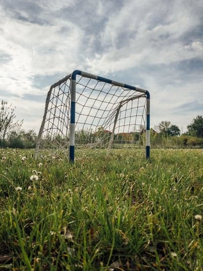 Abandoned Soccer Goal in Overgrown Field Under Cloudy Sky