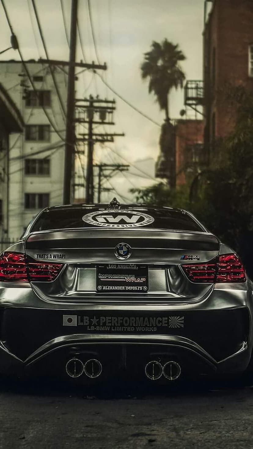 Silver satin BMW M4 with a widebody kit parked in an urban alley beneath power lines and a distant palm tree.