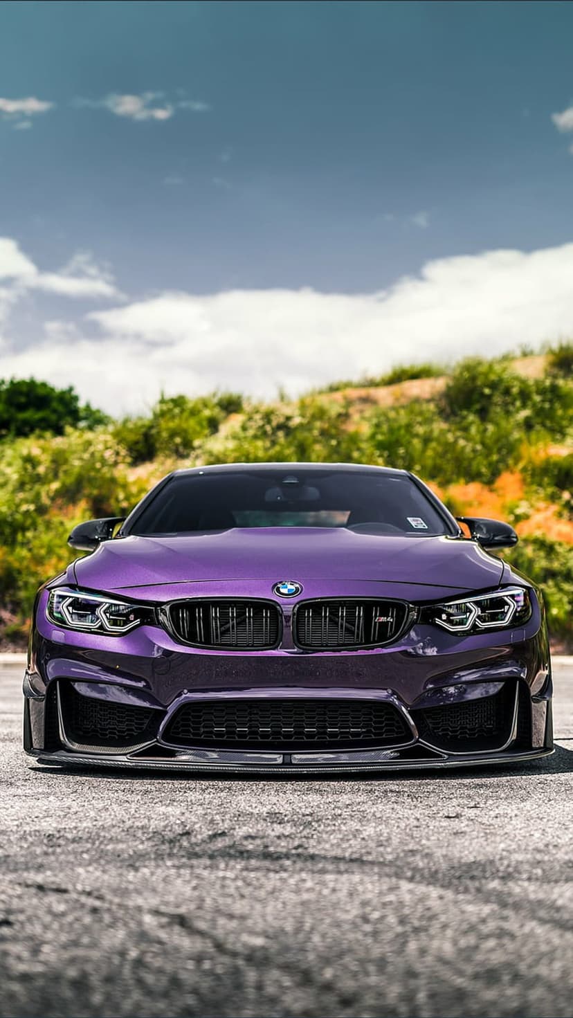 Purple BMW M4 coupe parked on asphalt with lush green foliage and a blue cloudy sky in the background.