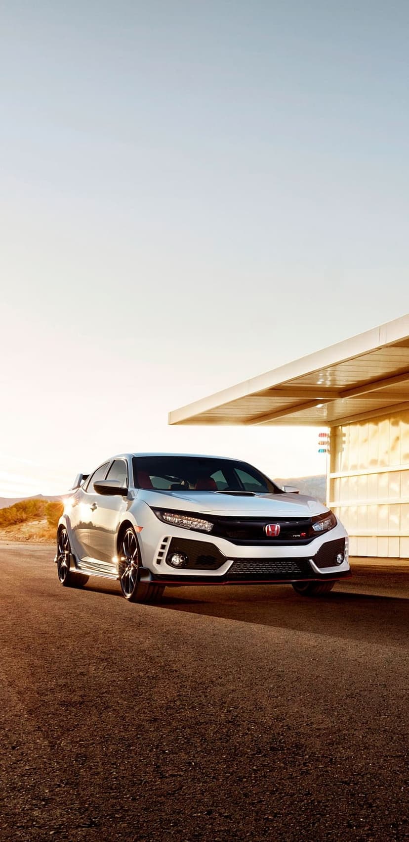 White Honda Civic Type R hatchback parked on asphalt beneath a modern shade structure in a sunlit desert setting.