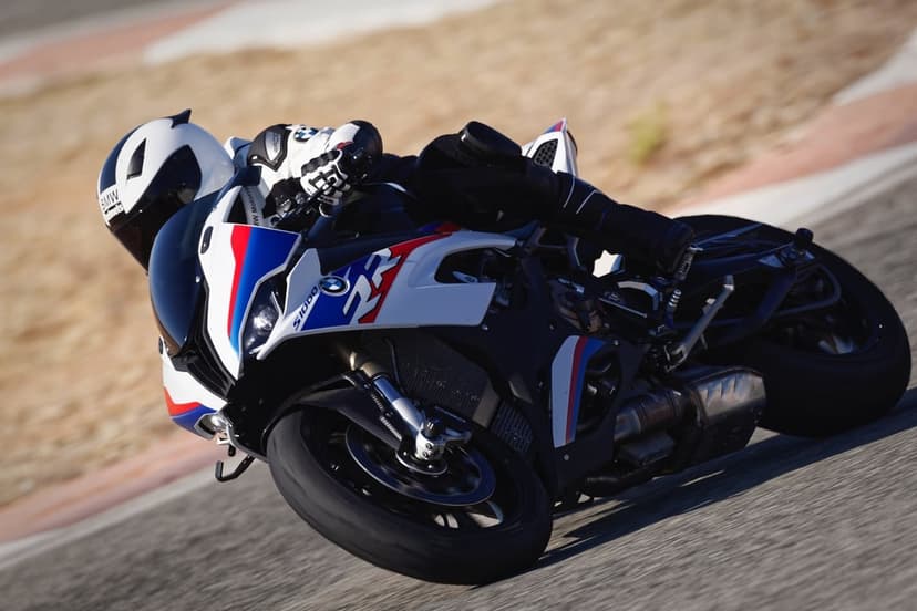 BMW S1000RR motorcycle leaning sharply in a corner on a racetrack with a rider in white and black gear.