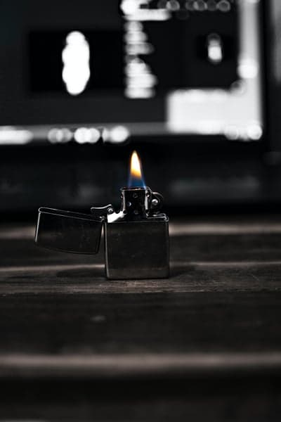Lighter with flame on wooden table, blurred background