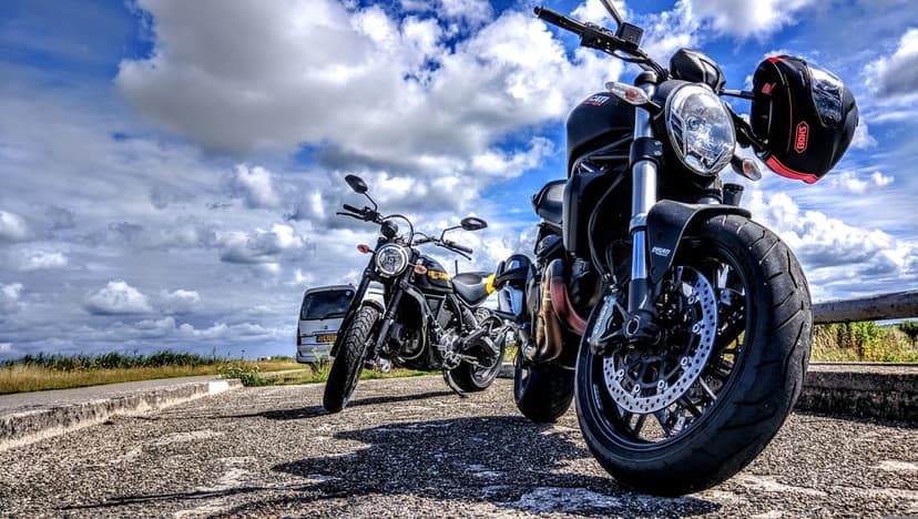 Two motorcycles park on an asphalt road featuring chrome details and a scenic blue sky with fluffy white clouds.