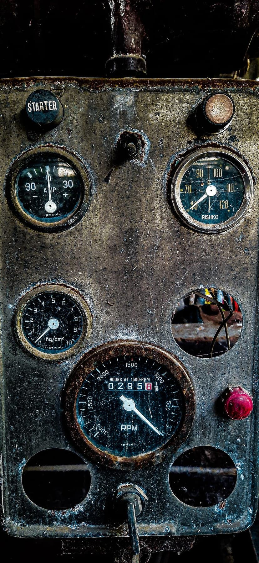 Weathered engine control panel with rusted metal surfaces, analog circular gauges, and a red starter button.