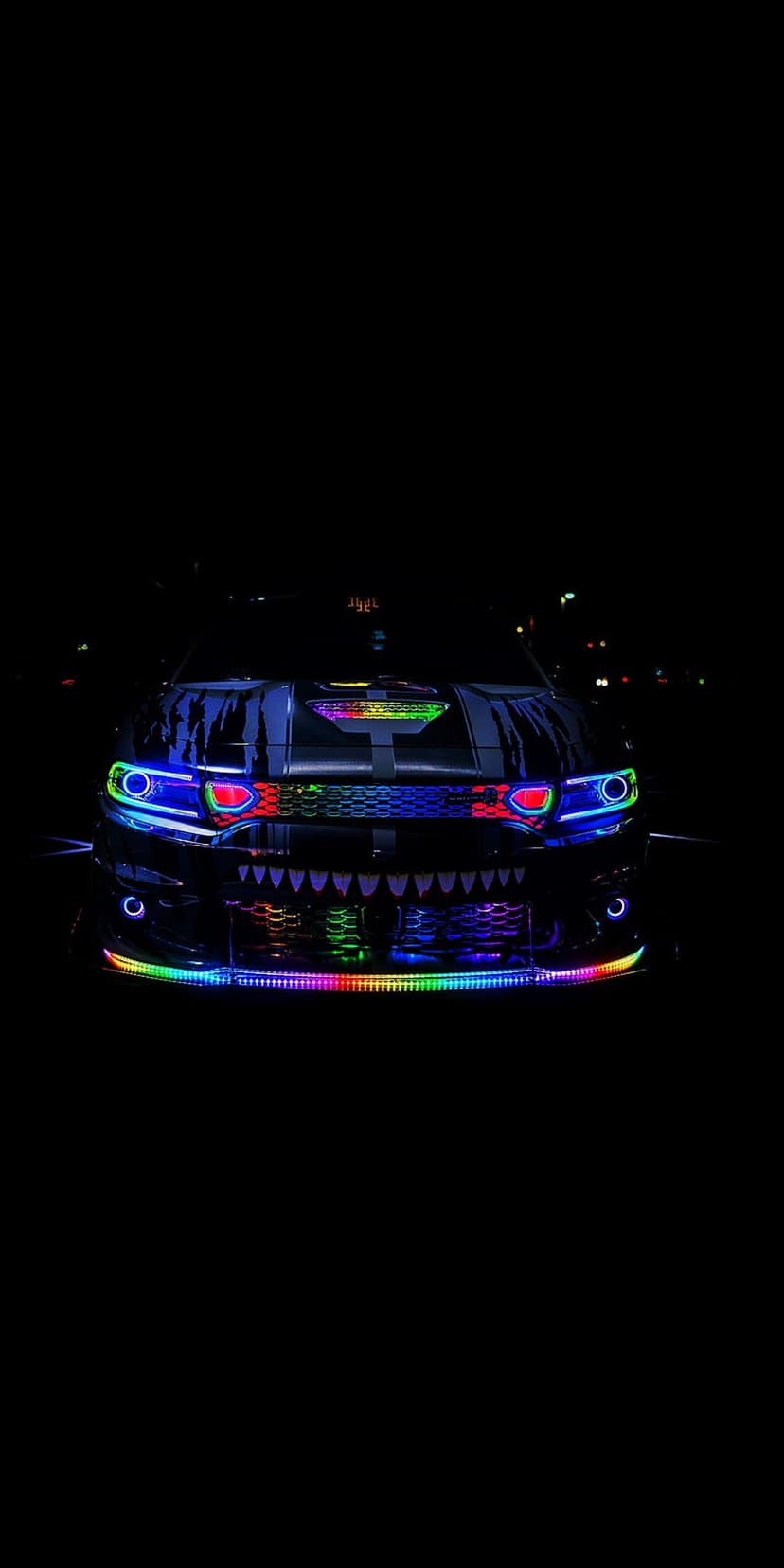 Dodge Charger with neon LED lights illuminating its front grille and headlights in a dark nighttime setting.