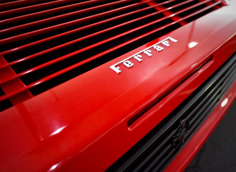 Silver Ferrari horse badge mounted on a red car body with horizontal air louvers and glossy paint reflections.