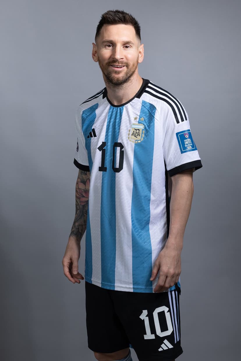 Lionel Messi wearing an Argentina striped jersey and number ten shorts against a solid grey studio background.