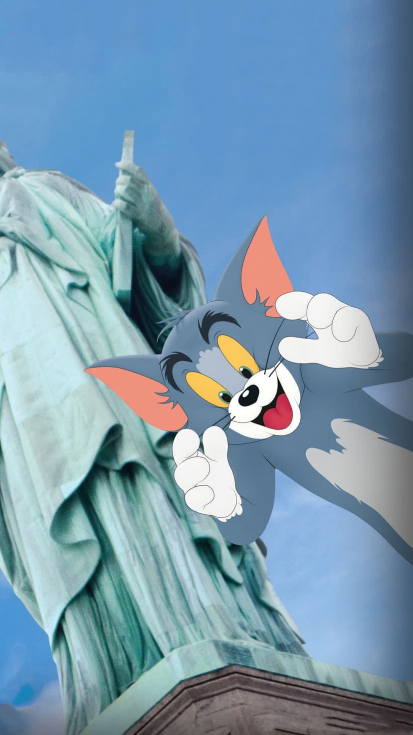 Tom the Cat posing in front of the Statue of Liberty with a clear blue sky and calm water in the background.