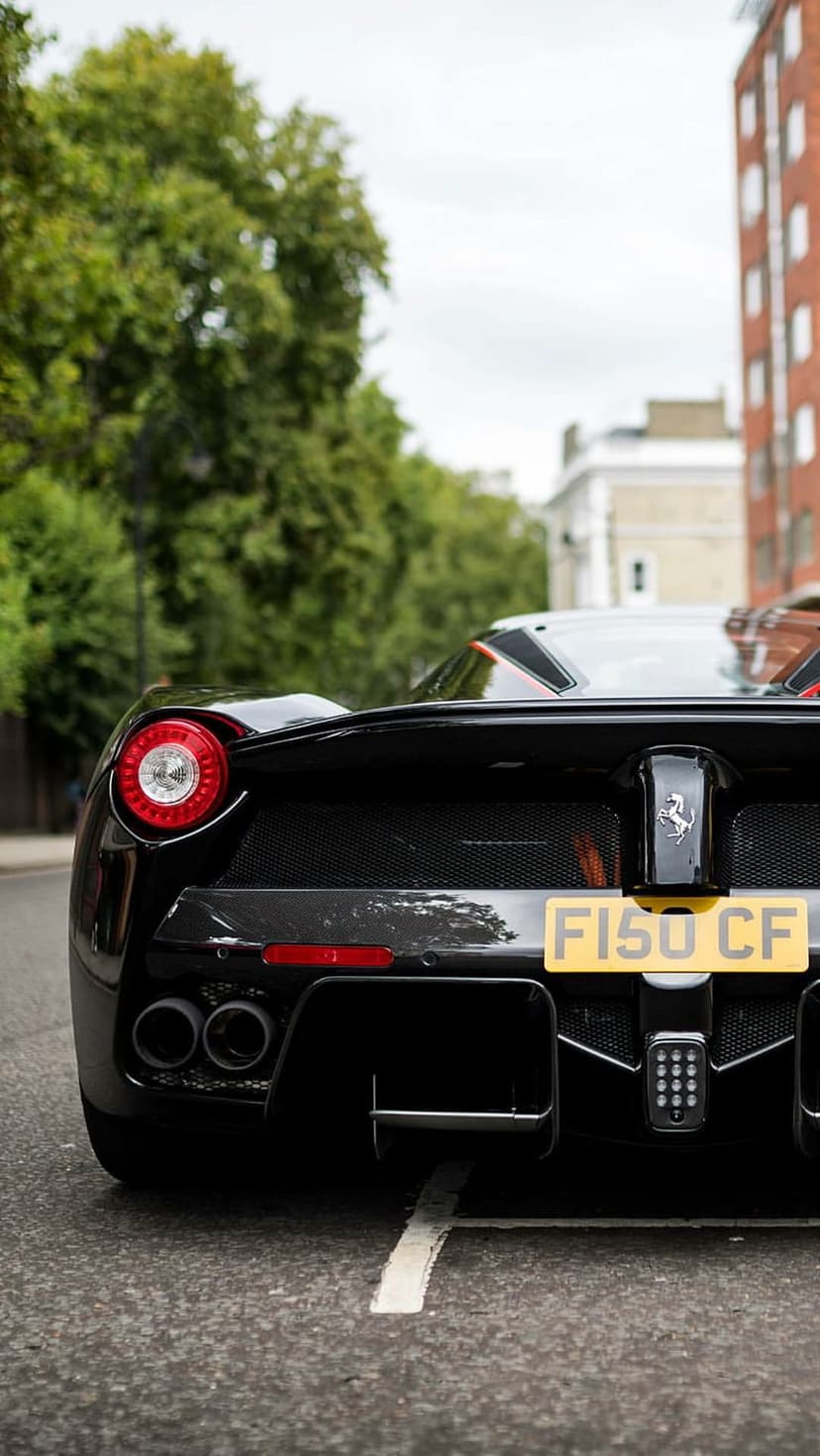 Black Ferrari LaFerrari rear view showing round taillights, quad exhaust pipes, and a license plate on a street.