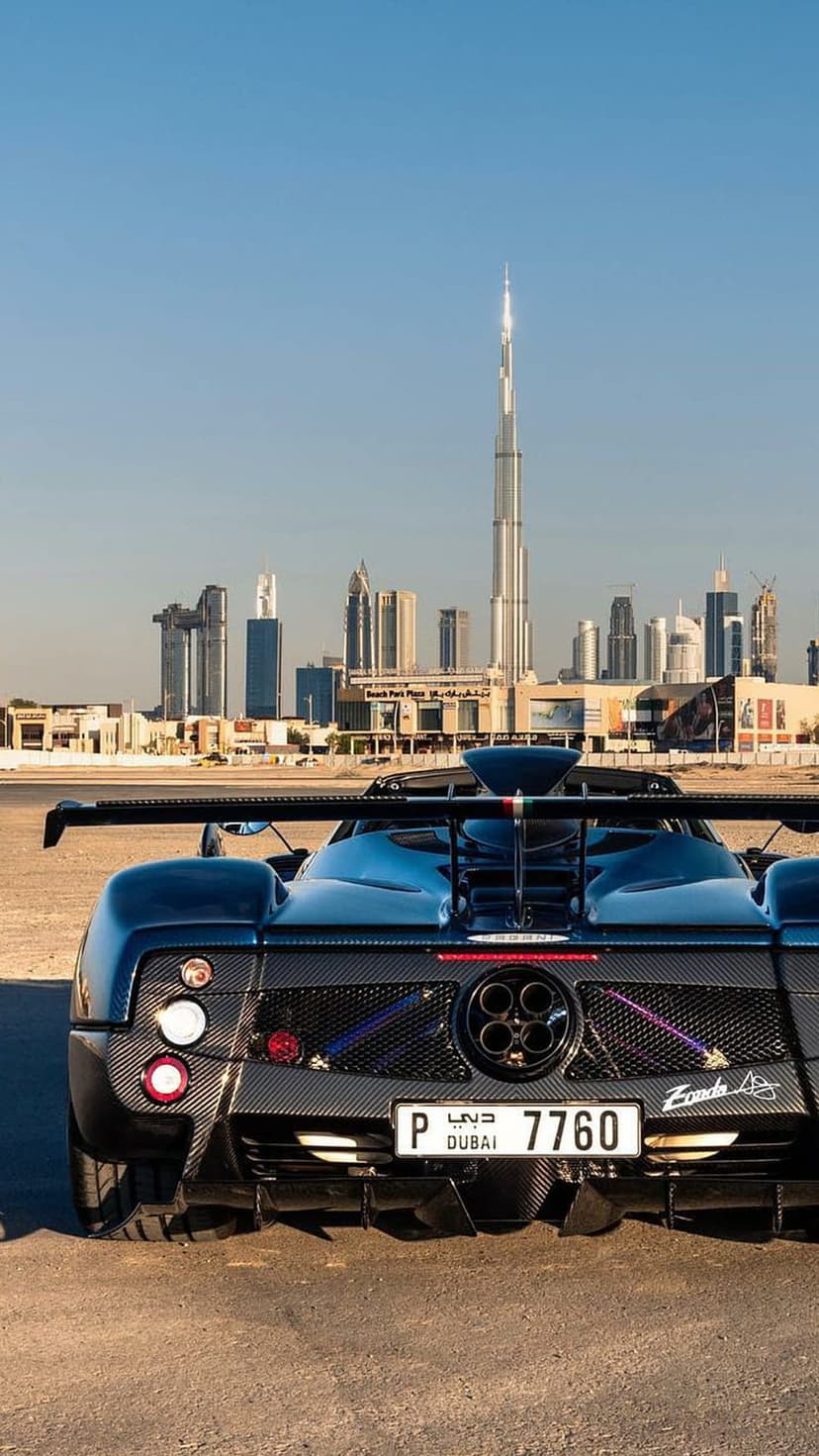 Blue Pagani Zonda rear view parked on desert sand with the Burj Khalifa and city skyscrapers in the distance.